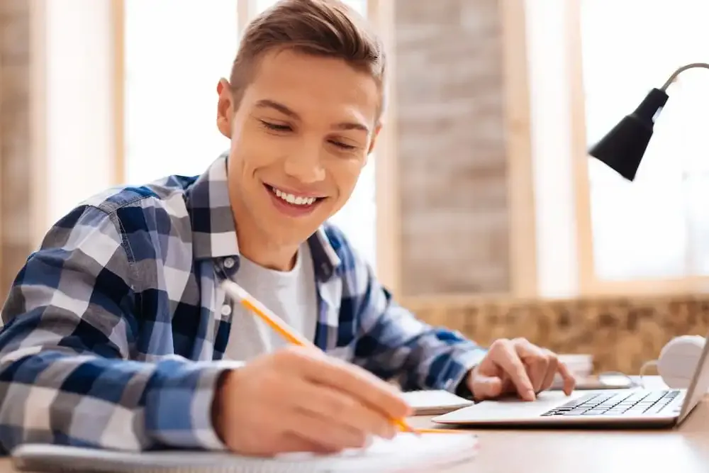 A young man is sitting at a computer, focused and engaged. He is working on a AS & A-LEVEL COMPUTER SCIENCE 9618 project, and he is clearly enjoying himself.