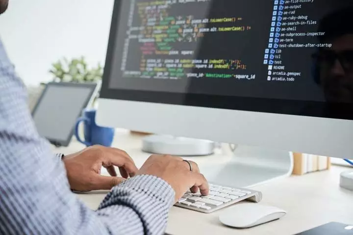 A young man is sitting at a computer, working on BACKEND PROGRAMMING. He is focused and determined, and he is clearly enjoying himself.